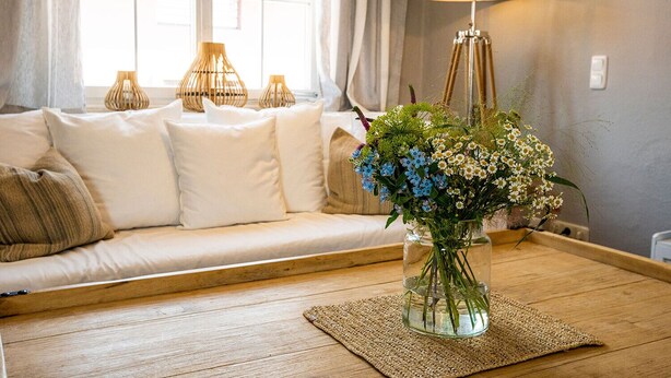 A cozy living room with a sofa, a vase of flowers, a lamp, and a view of the outside.