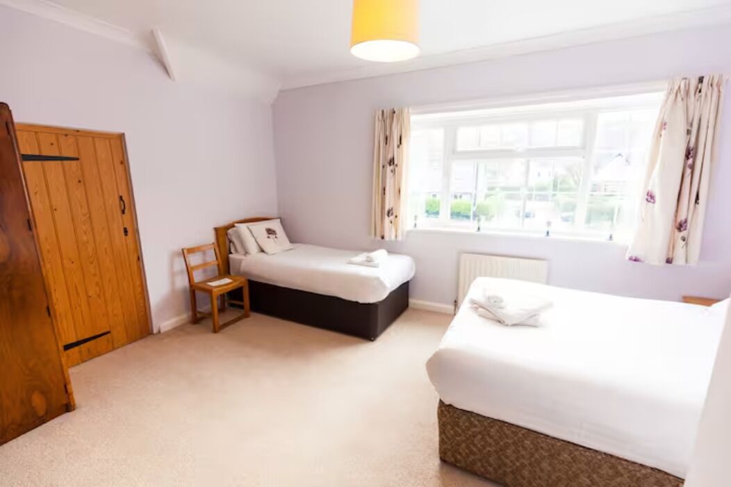 A bedroom with two beds, a wooden wardrobe, a chair, and a window with curtains.