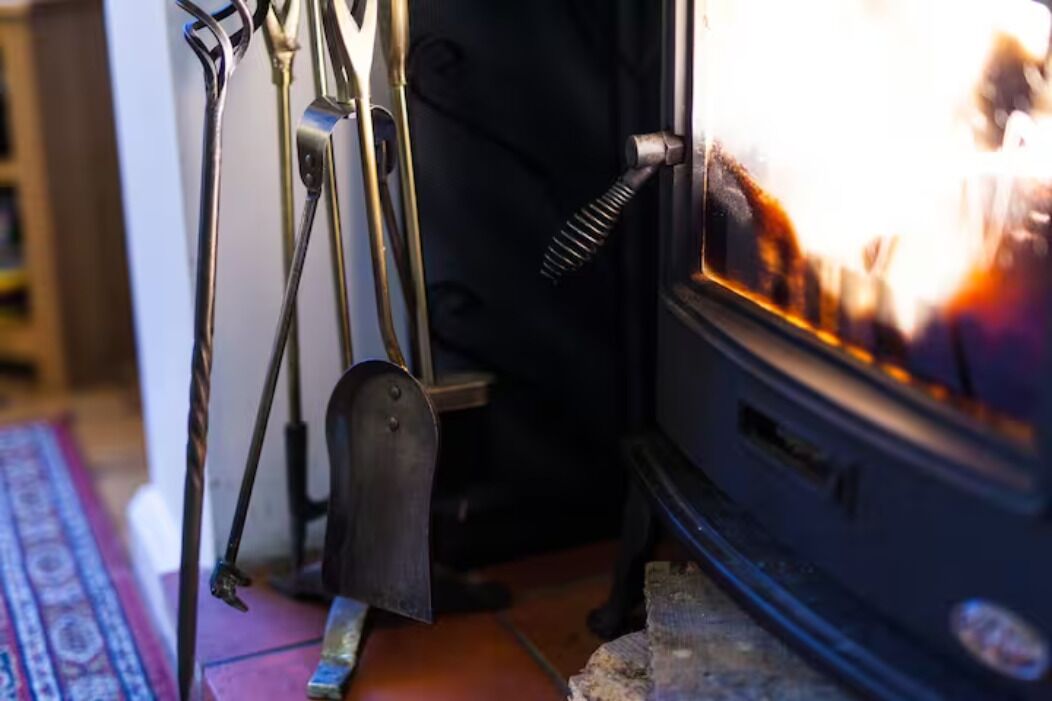 A wood-burning stove with a metal shovel and a metal hook.
