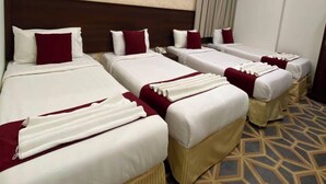 Een hotelkamer met vier bedden op een rij, een kamerbreed tapijt met een patroon en een modern plafondontwerp.