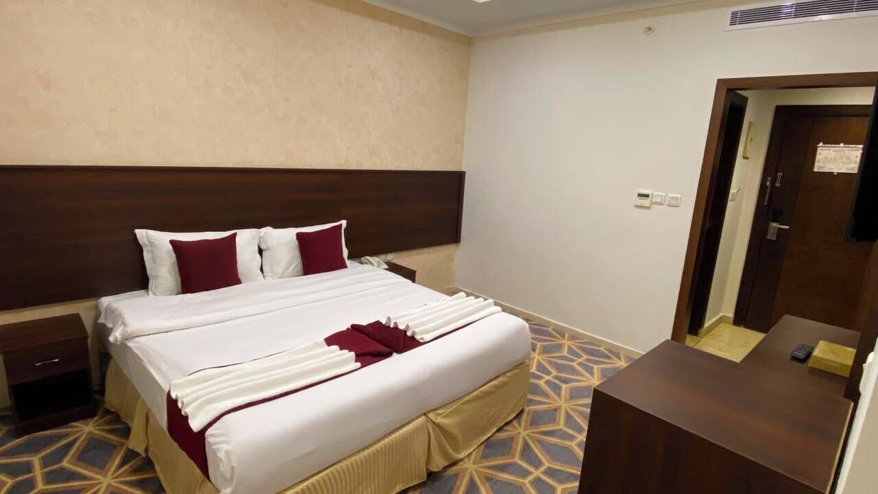 A hotel room with a large bed, a bedside table, a desk, and a door.
