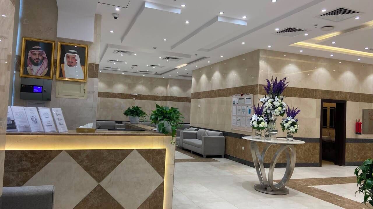 A hotel lobby with a reception desk, seating area, and decorative plants.