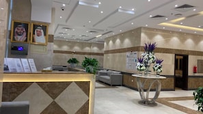 Un hall de hotel con mostrador de recepción, zona de estar y plantas decorativas.