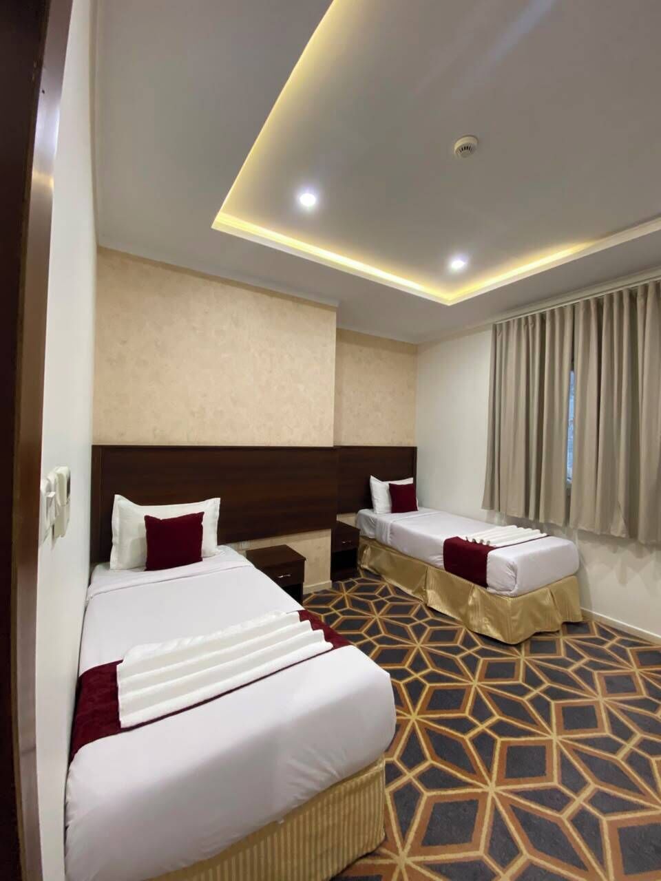 Une chambre d’hôtel avec deux lits, une moquette à motifs et un design moderne au plafond.