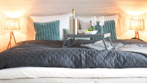 Ein Schlafzimmer mit einem Bett, einem Nachttisch mit Flasche und Gläsern sowie zwei Lampen.