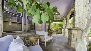 A covered outdoor seating area with wicker furniture, stone walls, and large windows. - Casa Alaïa | West Brickell | Sleeps 20 | Pool&Spa (Miami)
