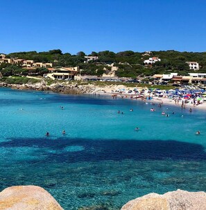 A coastal beach with clear blue waters, people swimming and sunbathing, and buildings in the background. - Accogliente Appartamento con Vista Mare (Santa Reparata)