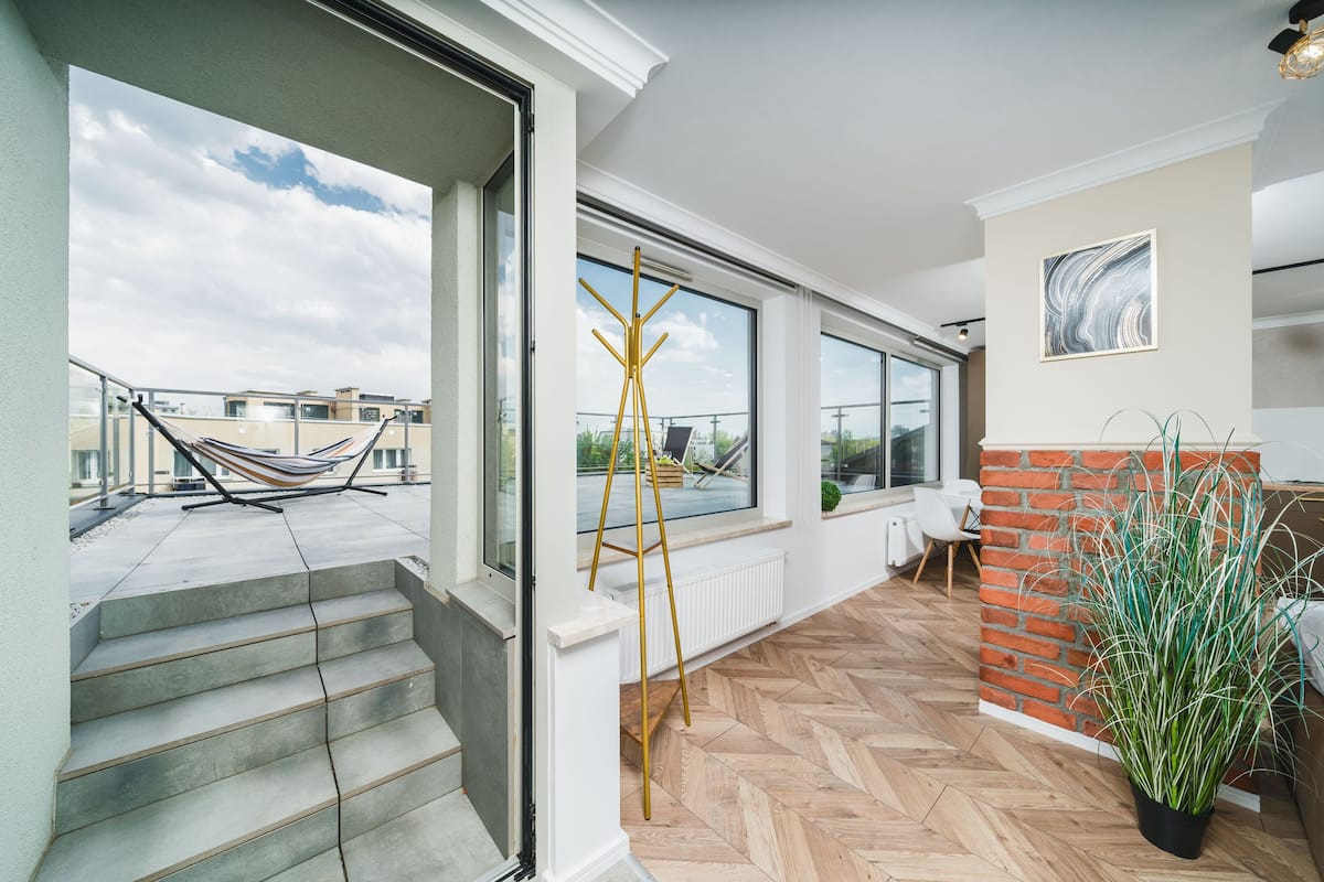 A modern interior with a herringbone floor, large windows, a brick accent wall, and a potted plant.