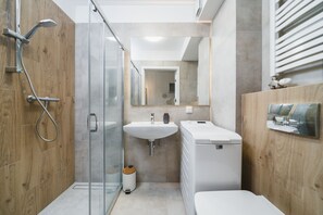 A modern bathroom with a glass shower enclosure, a sink, and a toilet. - APARTAMENTY NA DĘBNIKACH (Kraków)