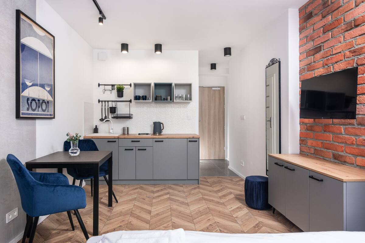 A modern kitchen with grey cabinets, a wooden herringbone floor, and a brick accent wall.