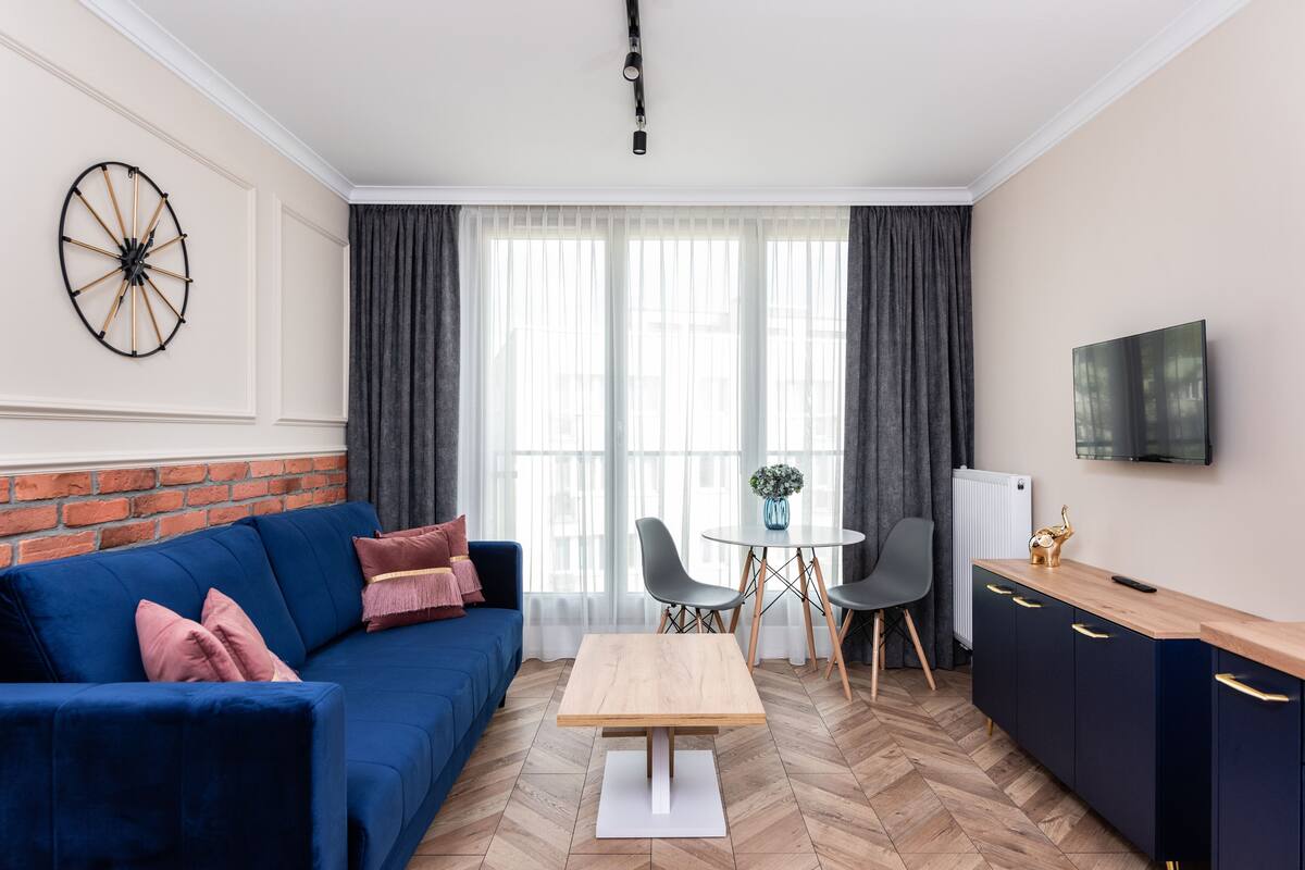 A modern living room with a blue sofa, a wooden coffee table, a TV, and a brick wall.