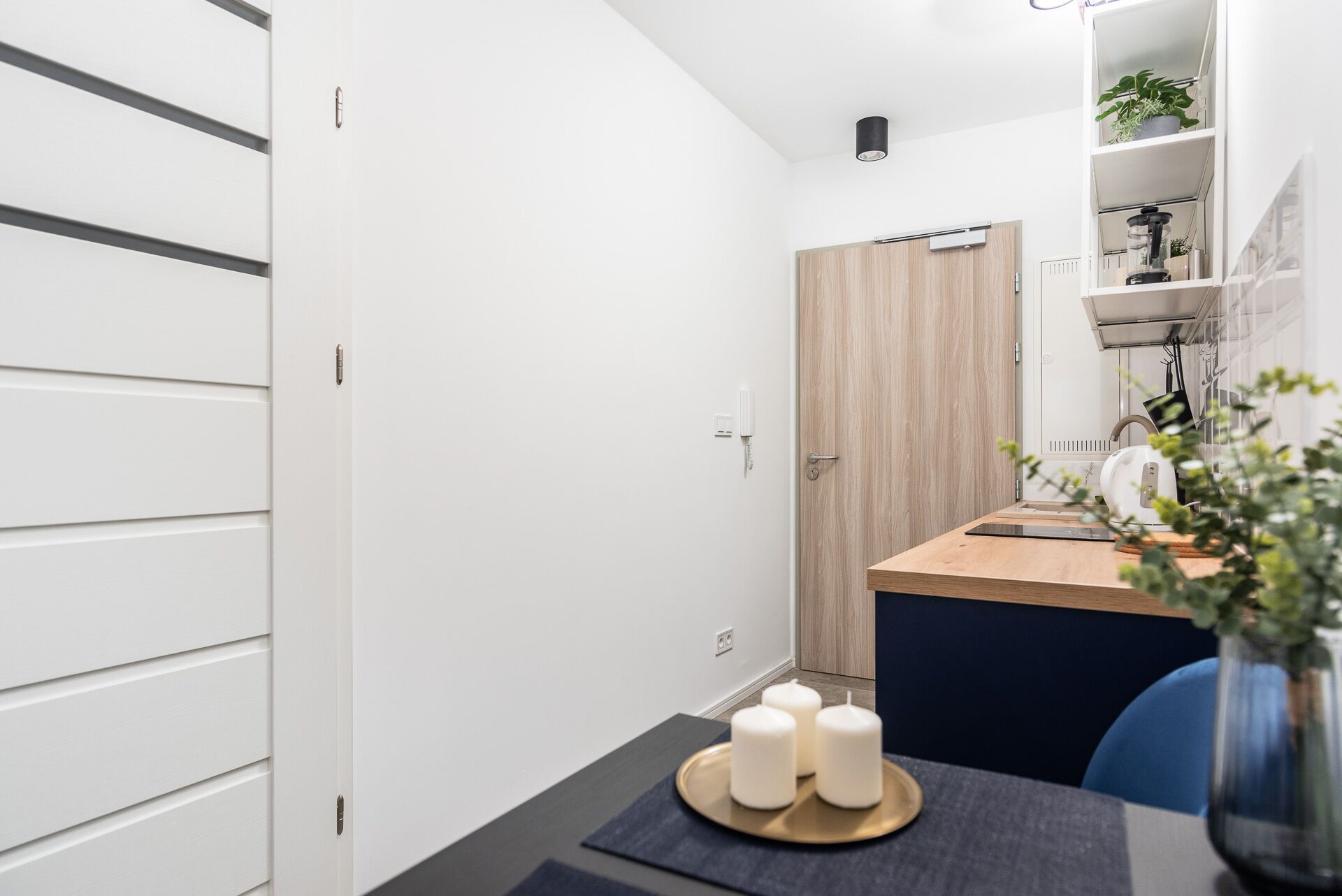 A modern kitchen with a wooden door, a countertop, and a table with candles.