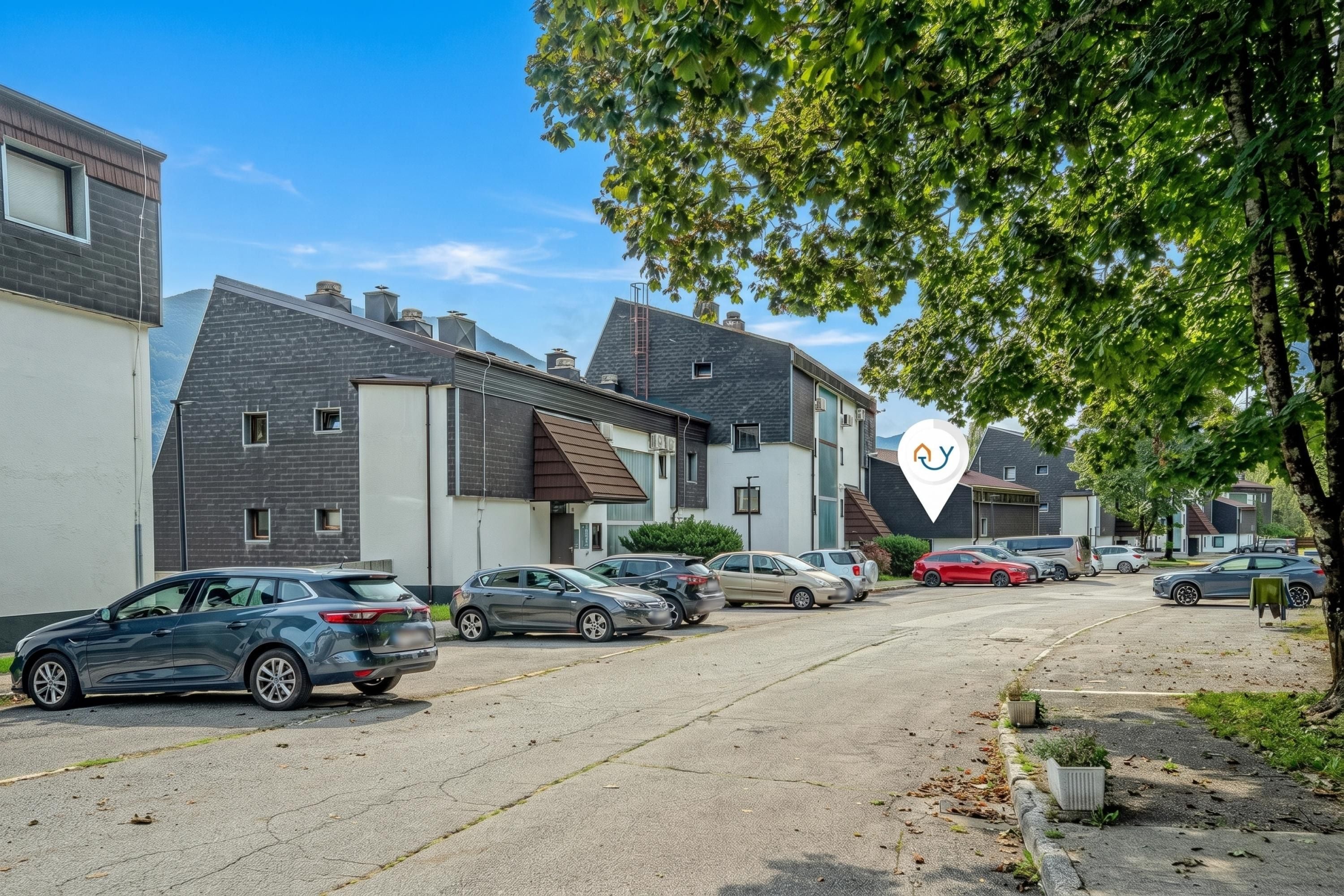 Una strada residenziale con case moderne, auto parcheggiate e cielo sereno.