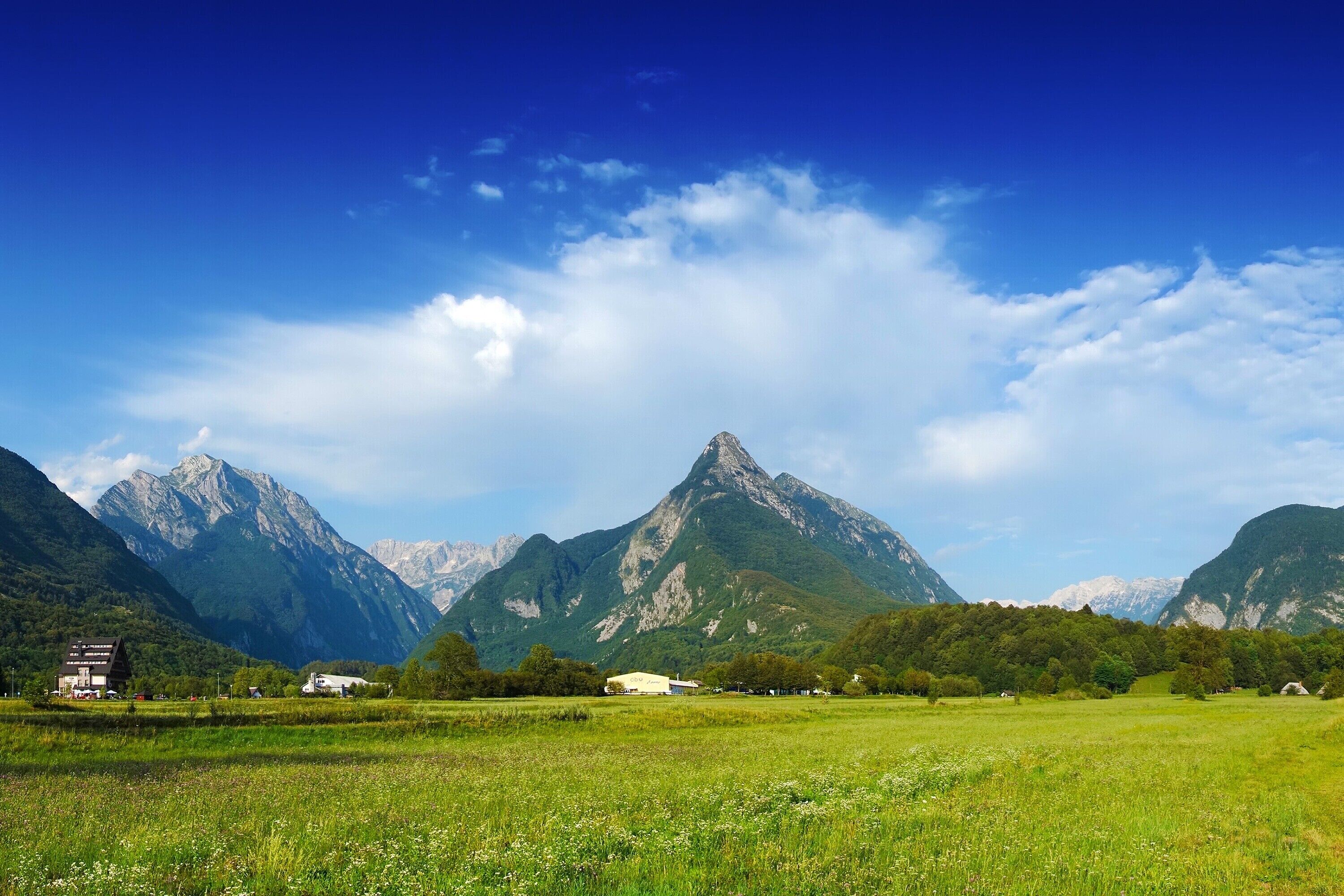 Eine Berglandschaft mit blauem Himmel, einer grünen Wiese und einigen Gebäuden im Vordergrund.