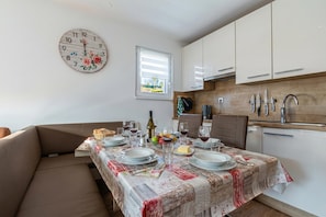 Uma sala de jantar com uma mesa posta para quatro pessoas, um relógio e uma janela com persianas.