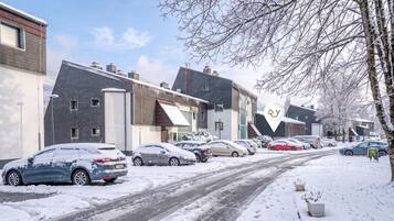 A residential street with houses, parked cars, and a snow-covered road.