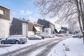 Une rue résidentielle bordée de maisons, avec des voitures garées et une chaussée recouverte de neige.