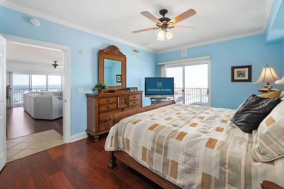 Un dormitorio con cama, cómoda, televisor y balcón con vistas.