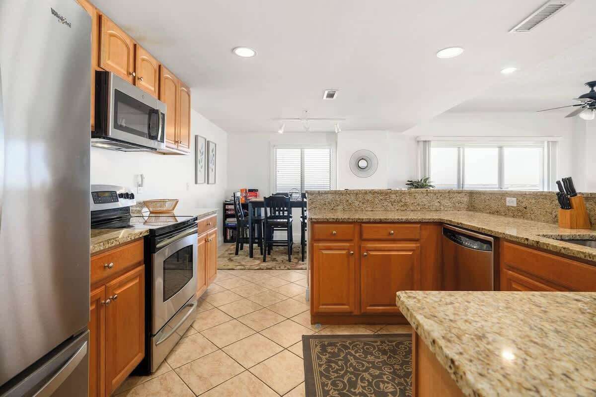 A modern kitchen with wooden cabinets, granite countertops, stainless steel appliances, and a dining area with a table and chairs.