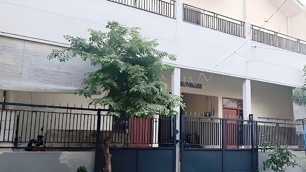 Ein zweistöckiges Gebäude mit geschlossenem Eingang, Blumentöpfen und einem Baum im Vordergrund.