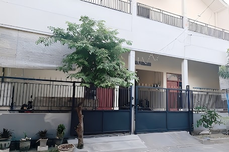 A two-story building with a gated entrance, potted plants, and a tree in the foreground.