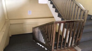 Eine Treppe mit Metallgeländer, die zu einer Zwischenebene mit weißer Wand und einem kleinen Schild führt.