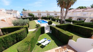 Um pátio com piscina, sebes bem aparadas e área de refeições com mobiliário de exterior.