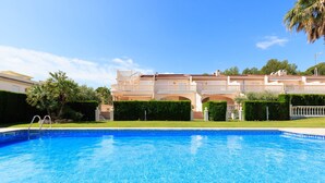 Uma piscina com superfície de água azul e límpida, rodeada por um gramado bem cuidado e um edifício grande com várias varandas ao fundo.