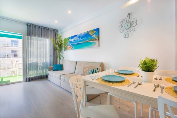 A modern living room with a dining area, a sofa, a painting, and a clock on the wall.