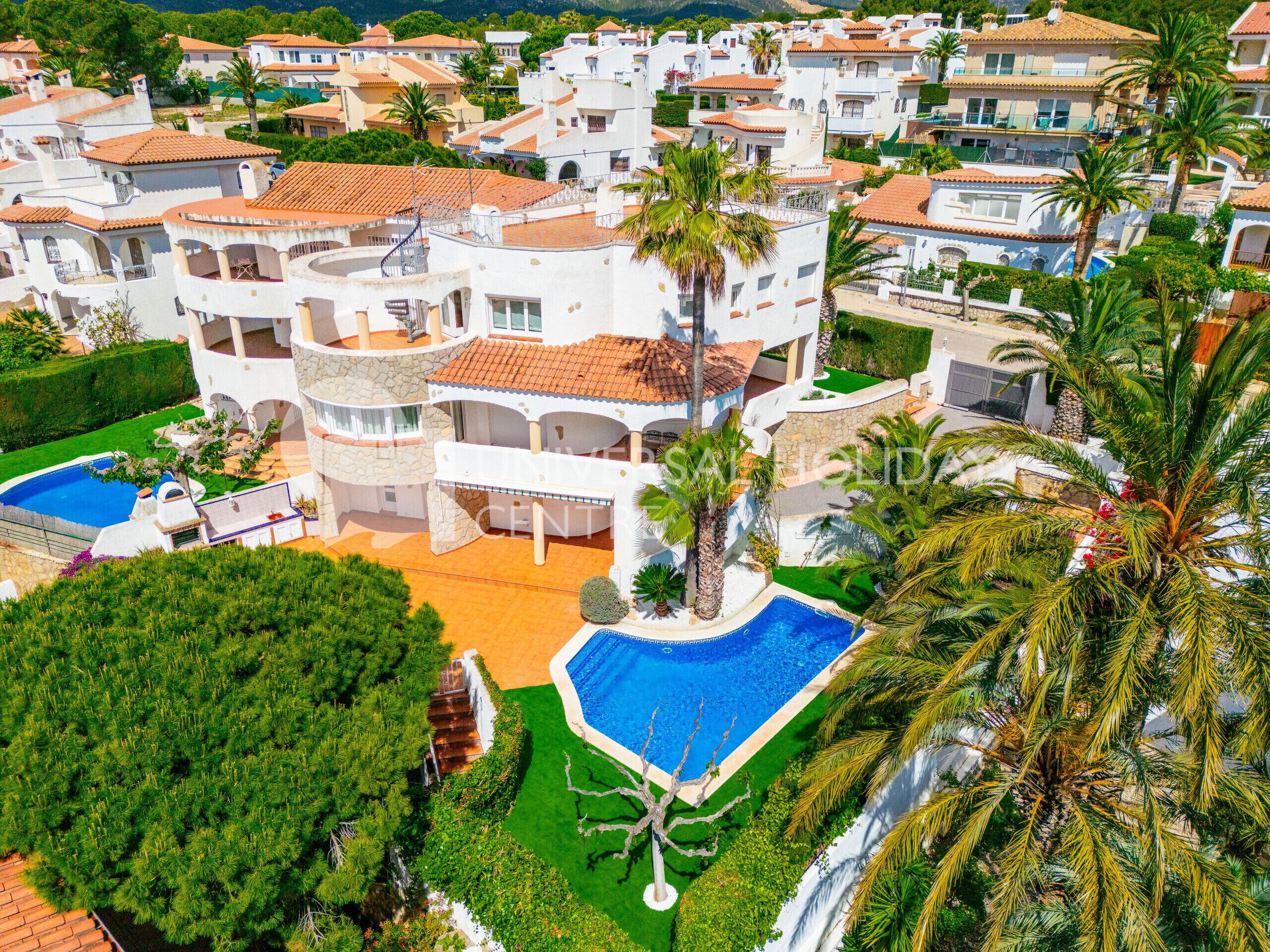 A multi-story residential building with a swimming pool, surrounded by lush greenery and palm trees.
