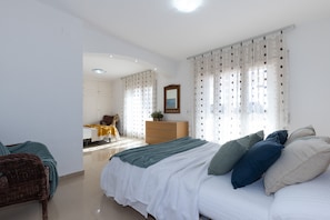 Relax in a serene bedroom with a large bed, dresser, and wicker chair.