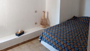 A bedroom with a bed, a bedside table, a vase, and a hanging light fixture. - Maisonnette Rustique (Le Garn)