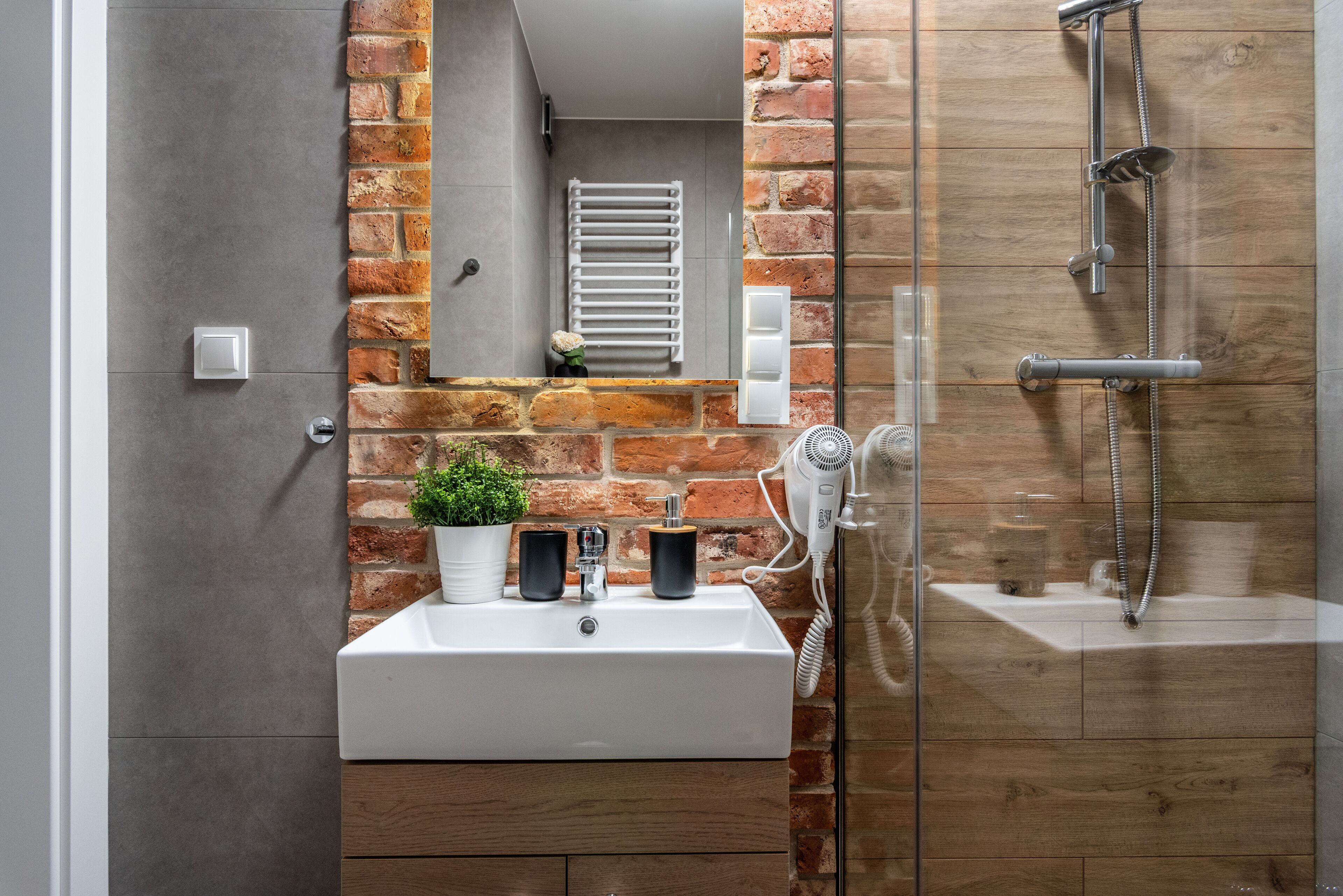 Un baño con un lavabo blanco, un espejo, toallero, cabezal de ducha de mano y un box de cristal.