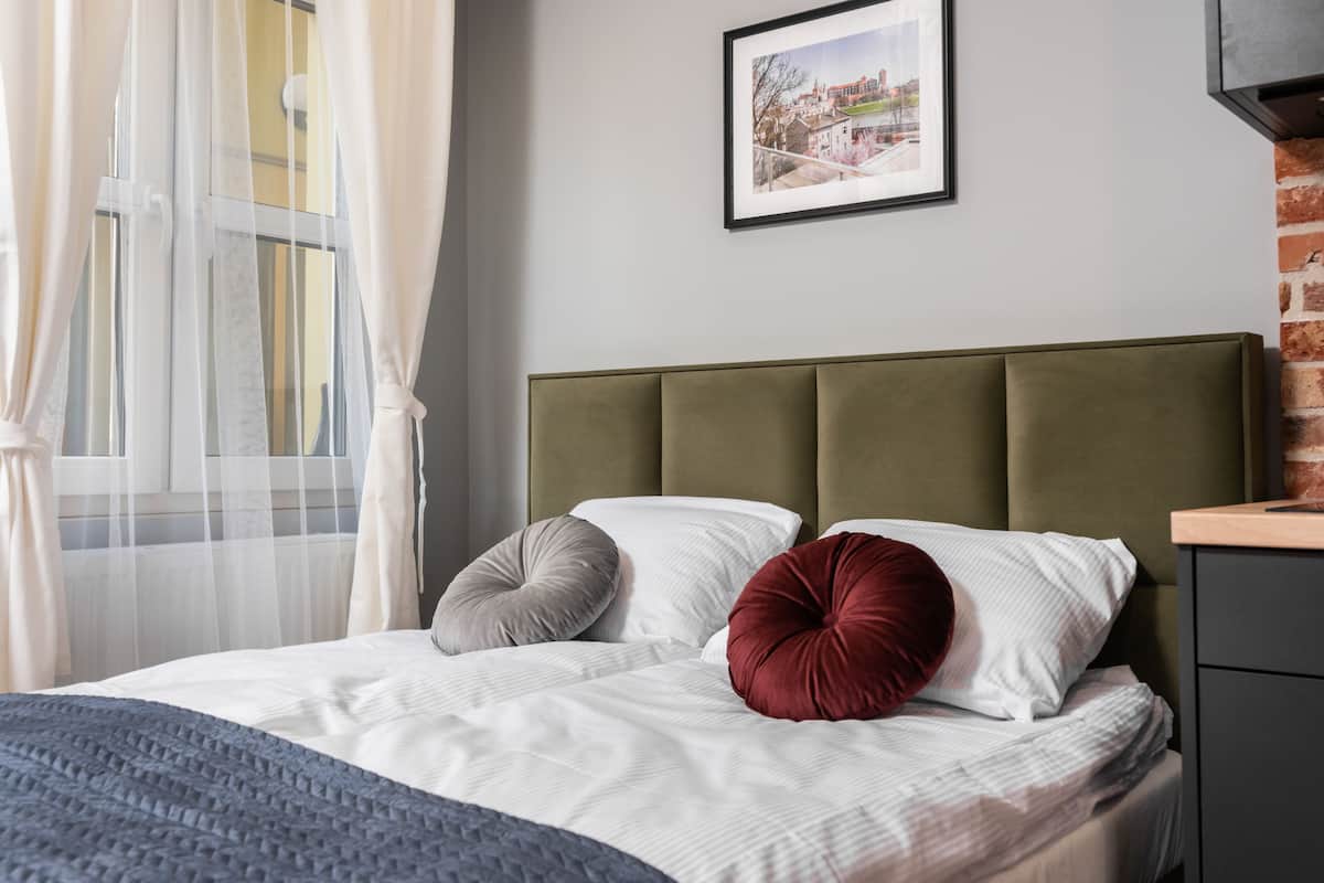 Cama bem arrumada com cabeceira verde, almofadas brancas e cinzentas, e um cobertor cinza.