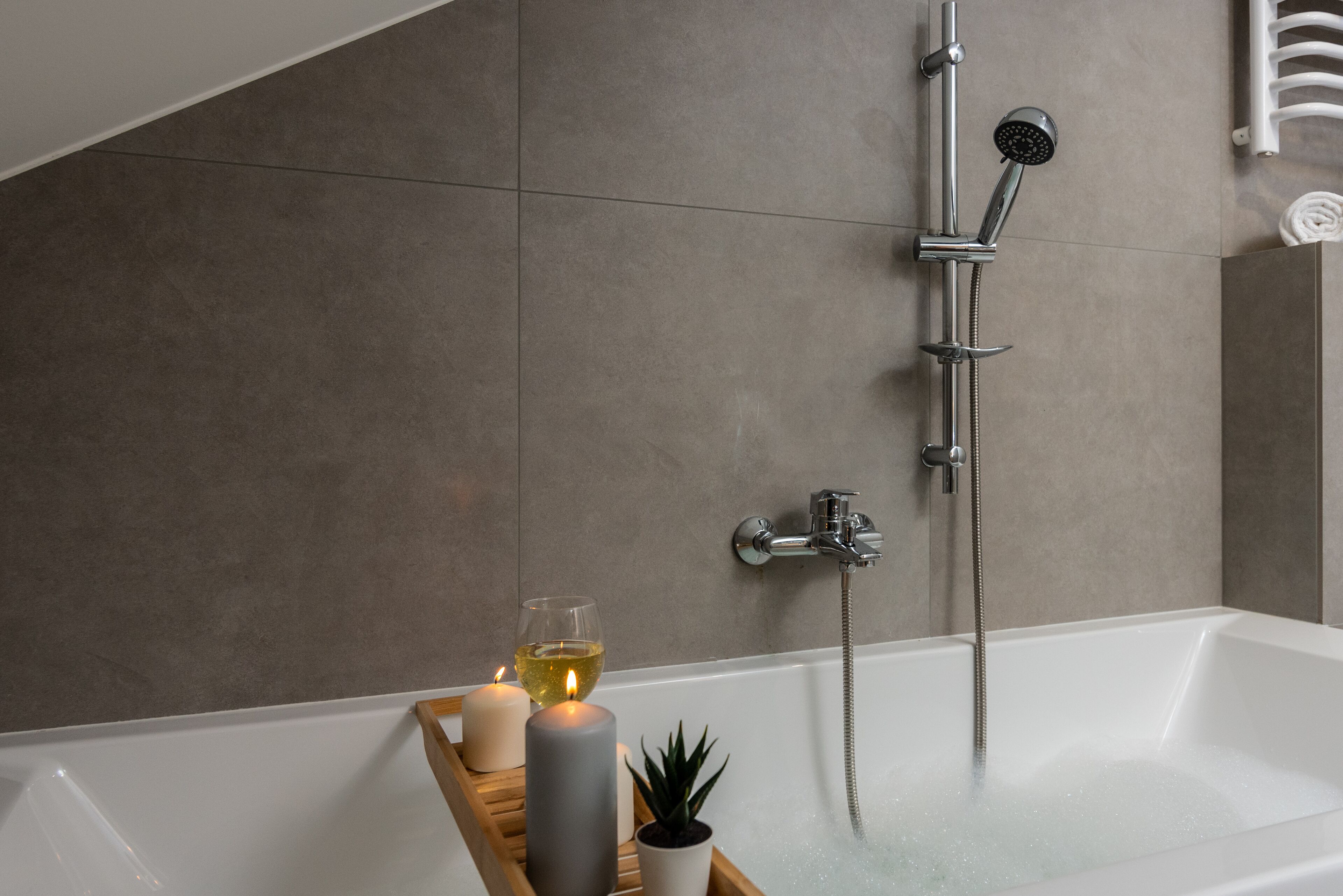 A modern bathroom with a bathtub, shower, and a wooden tray holding candles and a glass of wine.