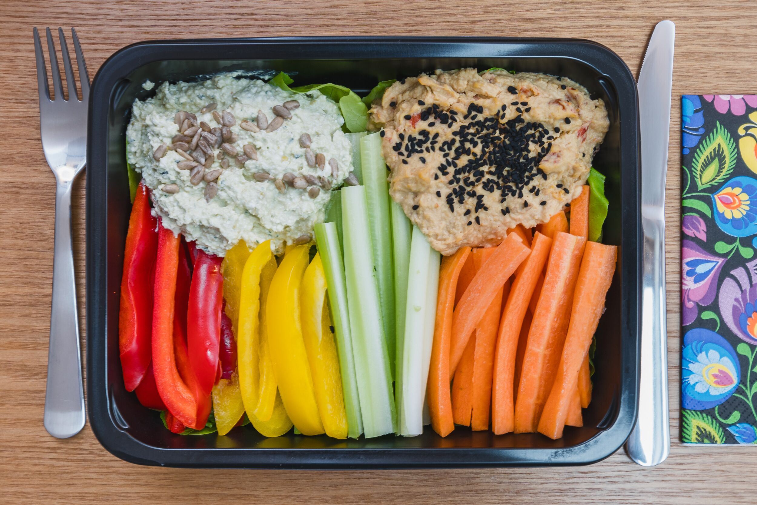 A meal with various vegetables and dips in a black tray.