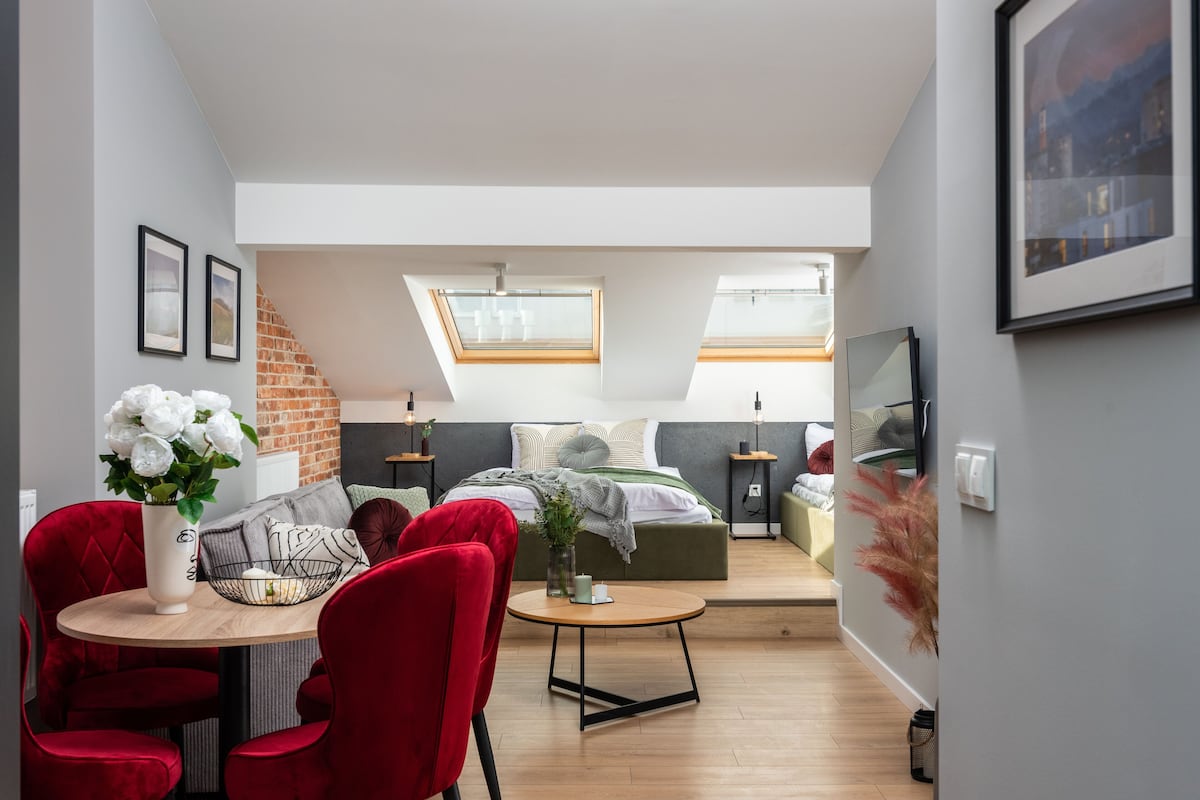 Apartamento moderno com quarto no estilo loft, sala de jantar com cadeiras vermelhas e uma pequena cozinha.