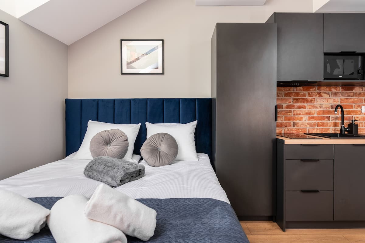 Quarto moderno com uma cama grande, cabeceira azul e área de cozinha com painel de parede de tijolos.