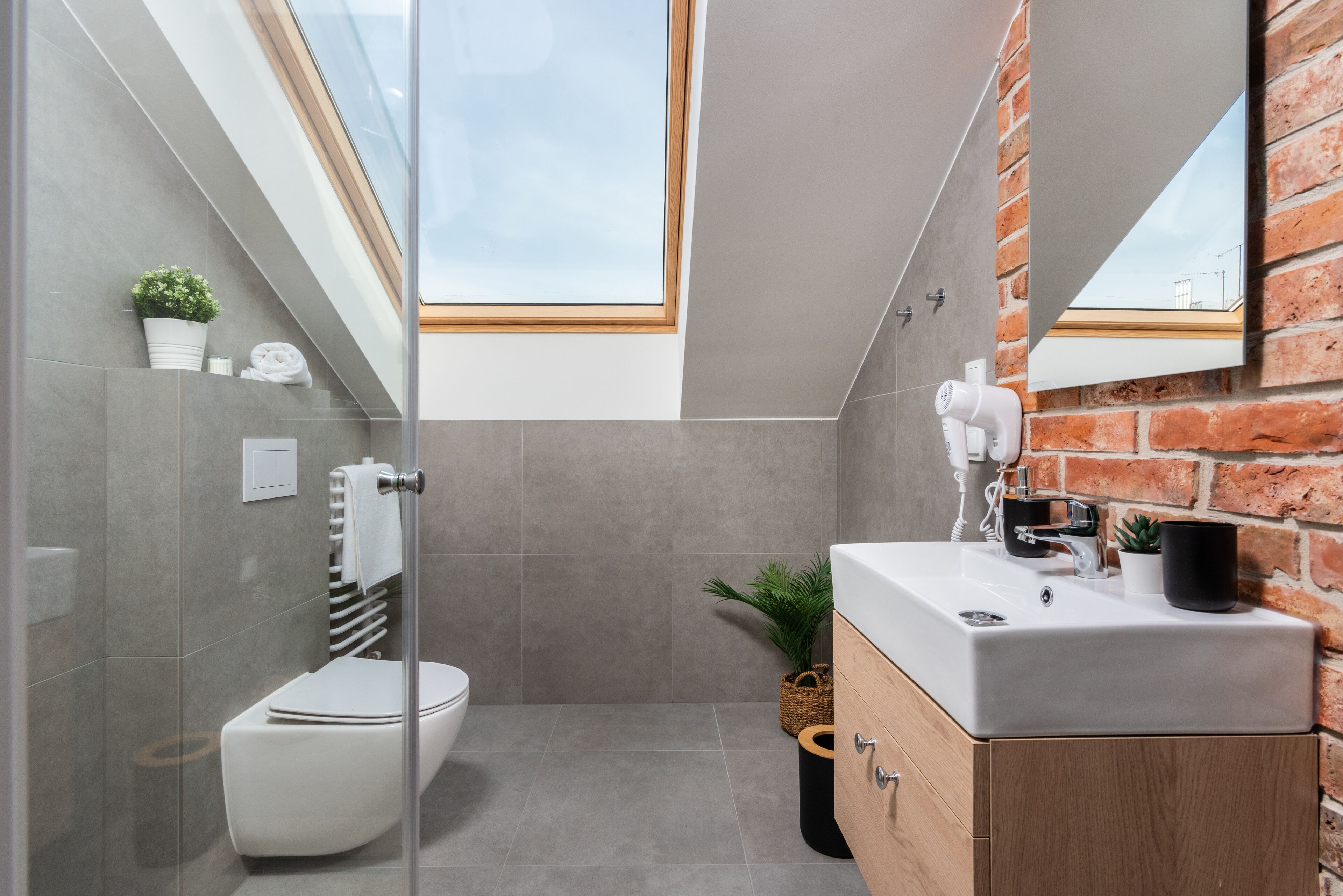 A modern bathroom with a glass-enclosed shower, a white toilet, a wooden vanity, and a brick wall.