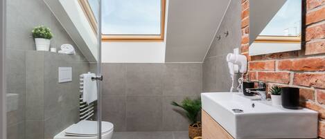 A modern bathroom with a glass-enclosed shower, a white toilet, a wooden vanity, and a brick wall.