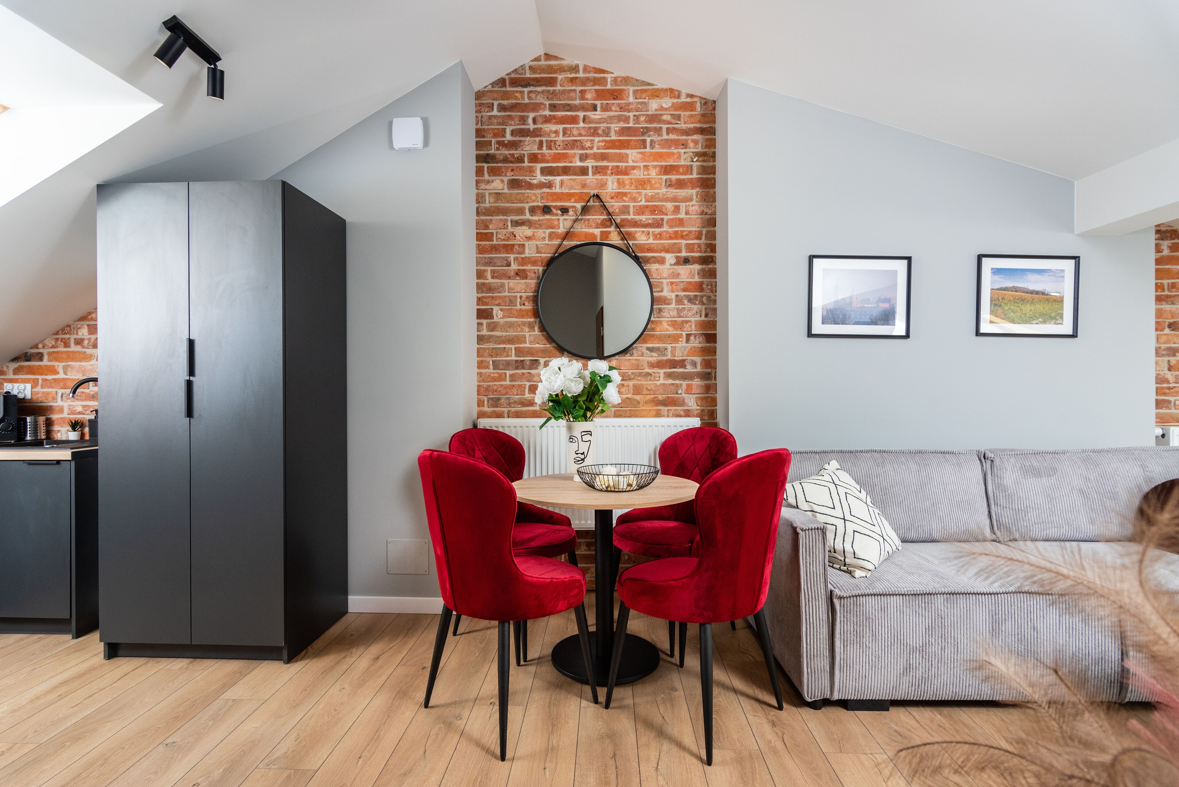 Una cocina moderna con pared de ladrillo, una mesa de comedor con sillas rojas y un sofá gris.