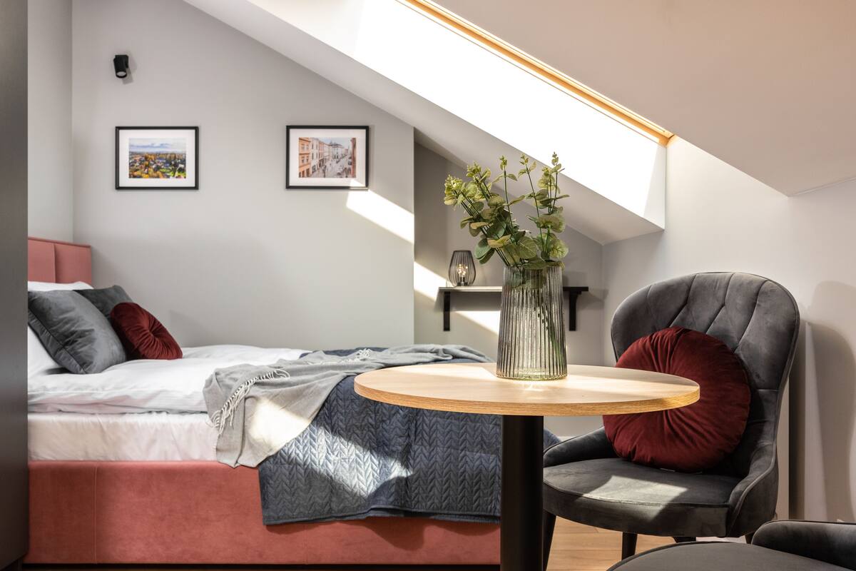 Um quarto moderno com cama estilo loft, uma mesa redonda de madeira com um vaso de flores e uma poltrona confortável.