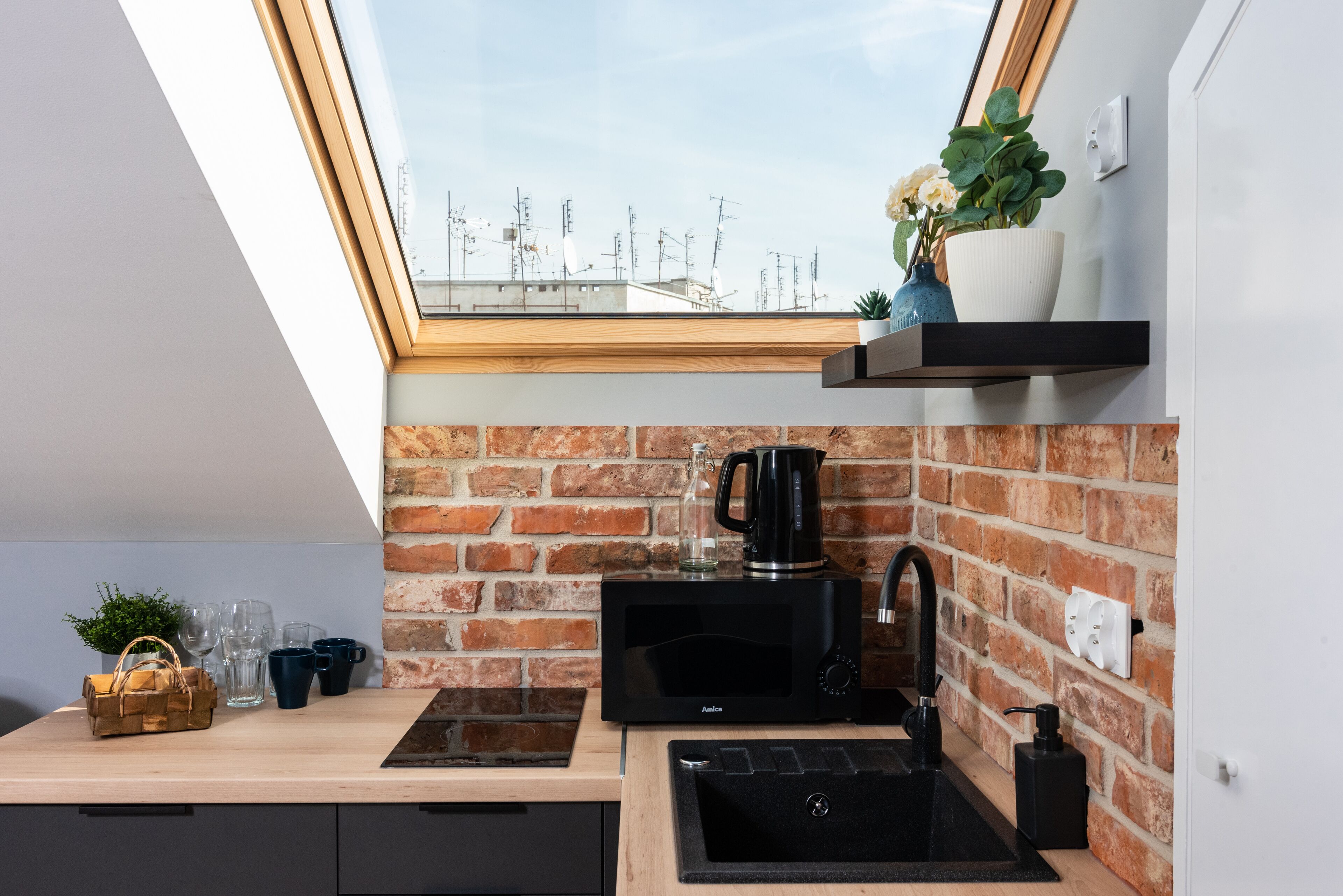 Eine moderne Küche mit Ziegelrückwand, einer schwarzen Mikrowelle, einem Spülbecken und einem Fenster mit Blick auf eine Stadtlandschaft.