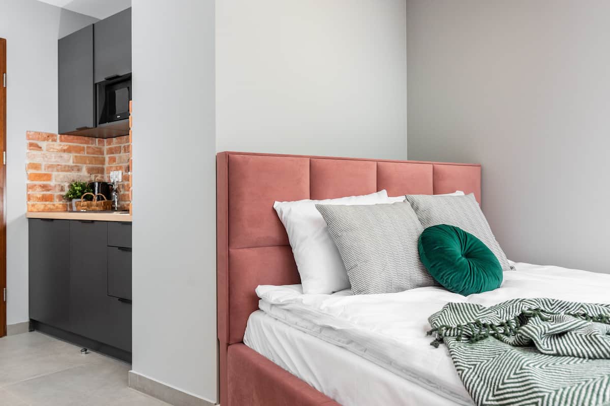 Quarto com cabeceira estofada em rosa, roupa de cama branca e almofada de destaque verde.