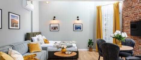 Una sala de estar moderna con un sofá gris, una mesa de centro redonda y una zona de comedor con pared de ladrillo y cortinas amarillas.