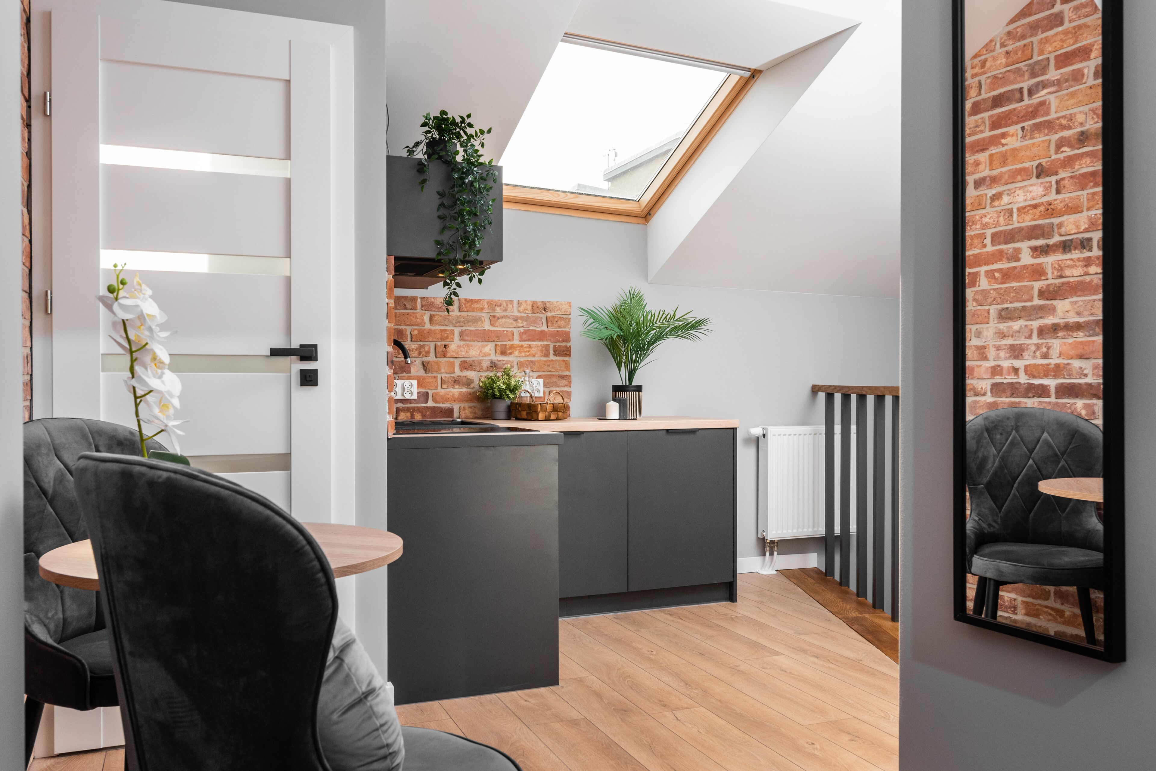 Una cocina moderna con tragaluz, pared de ladrillo y zona de comedor con una silla y una mesa negros.
