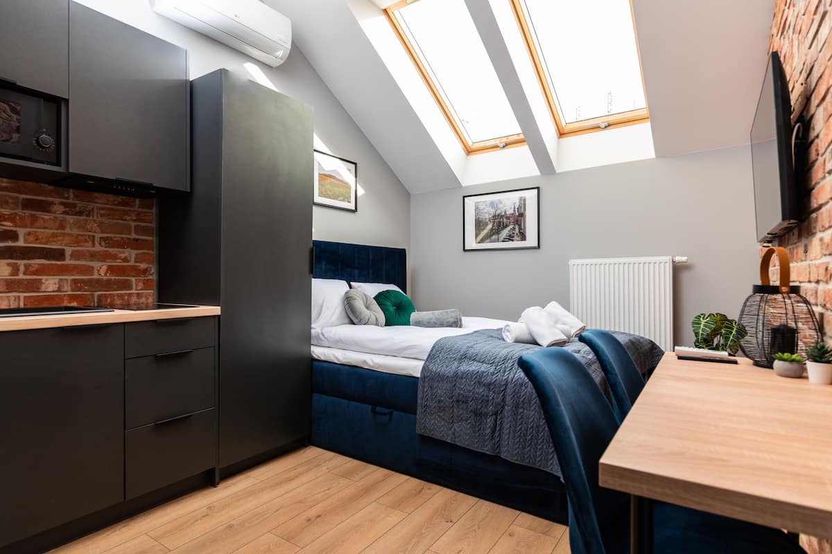 Quarto compacto com cama, escrivaninha e claraboia.