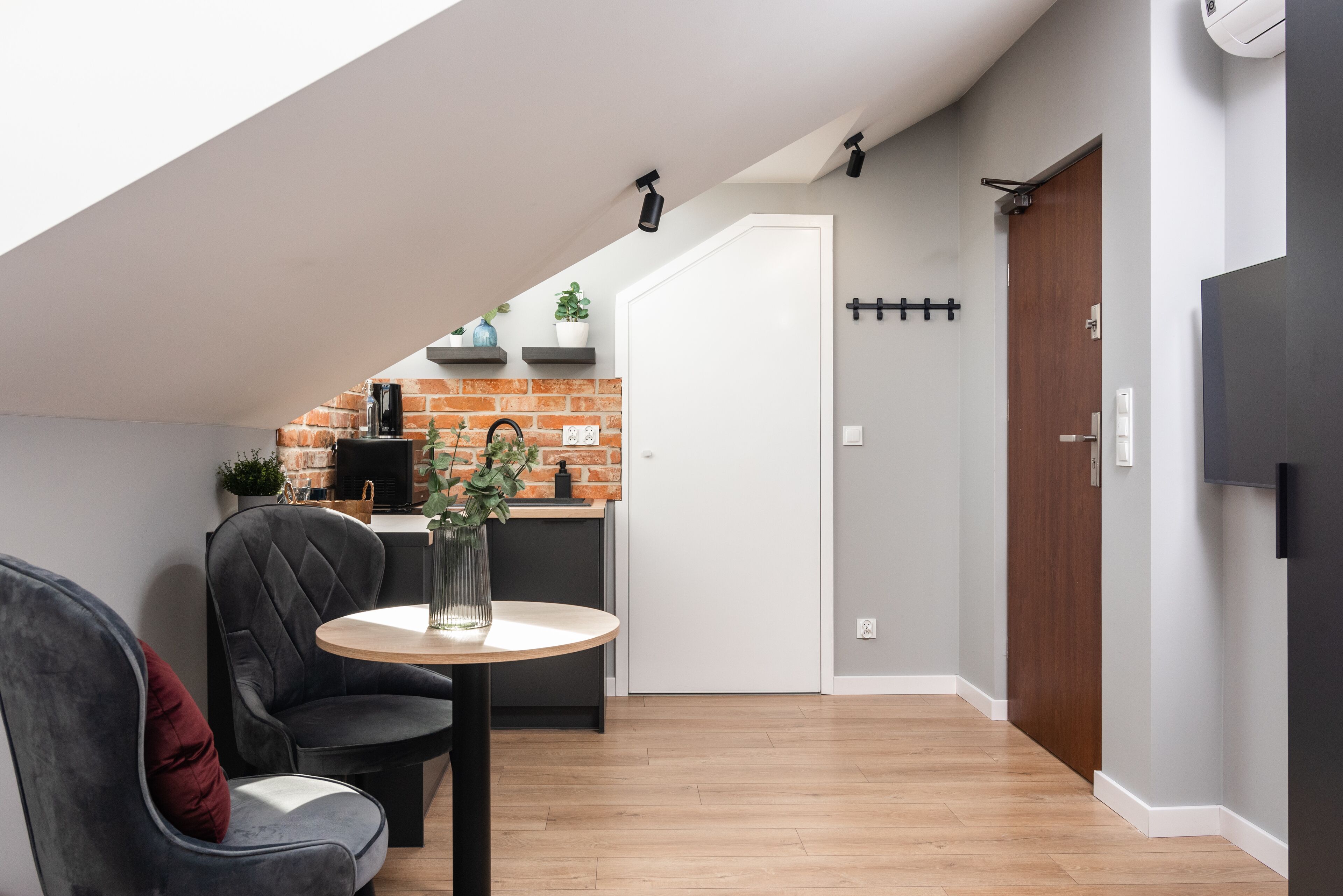 Een moderne loft met een keukenhoek, een meterkast met bakstenen achterwand, een eettafel met stoelen en een trap naar een hoger niveau.