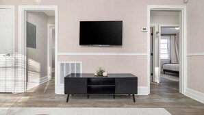 A modern living room with a flat-screen TV mounted on the wall, a dark wooden entertainment center, and a light-colored rug.