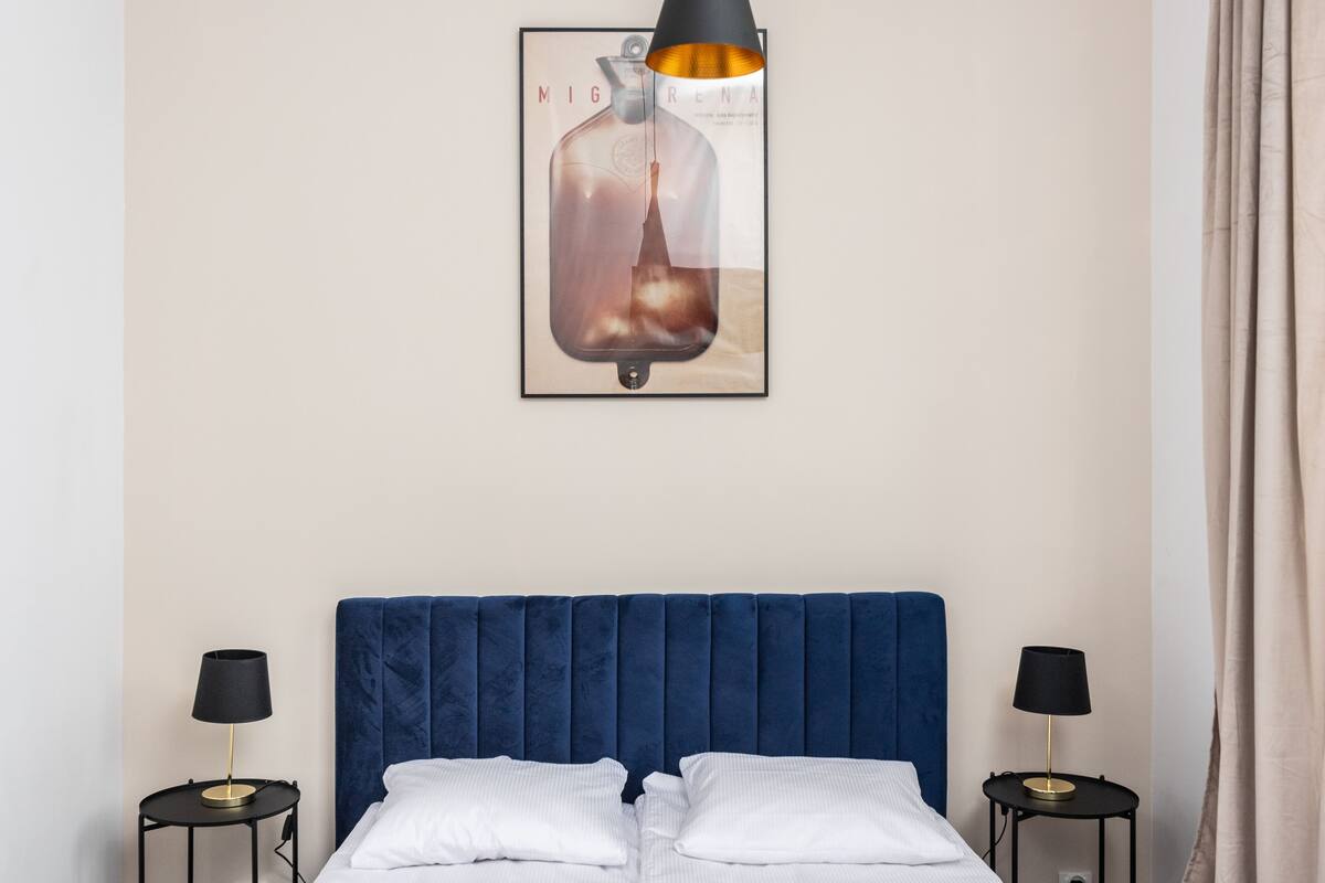 A bedroom with a blue headboard, two bedside tables with lamps, and a framed picture above the bed.